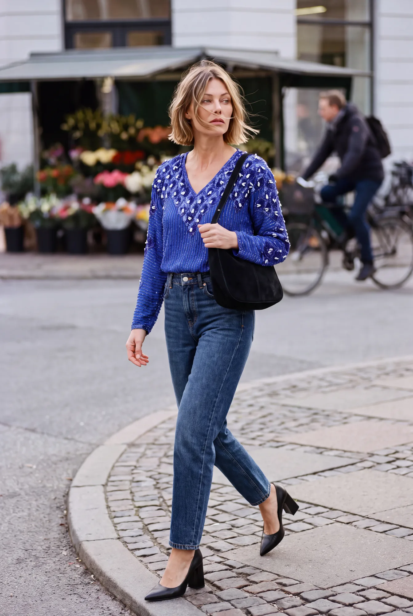 A blonde woman with a jaw-length bob walks on a cobblestone street wearing a blue beaded v-neck sequin top tucked into | After the Toast, Relover