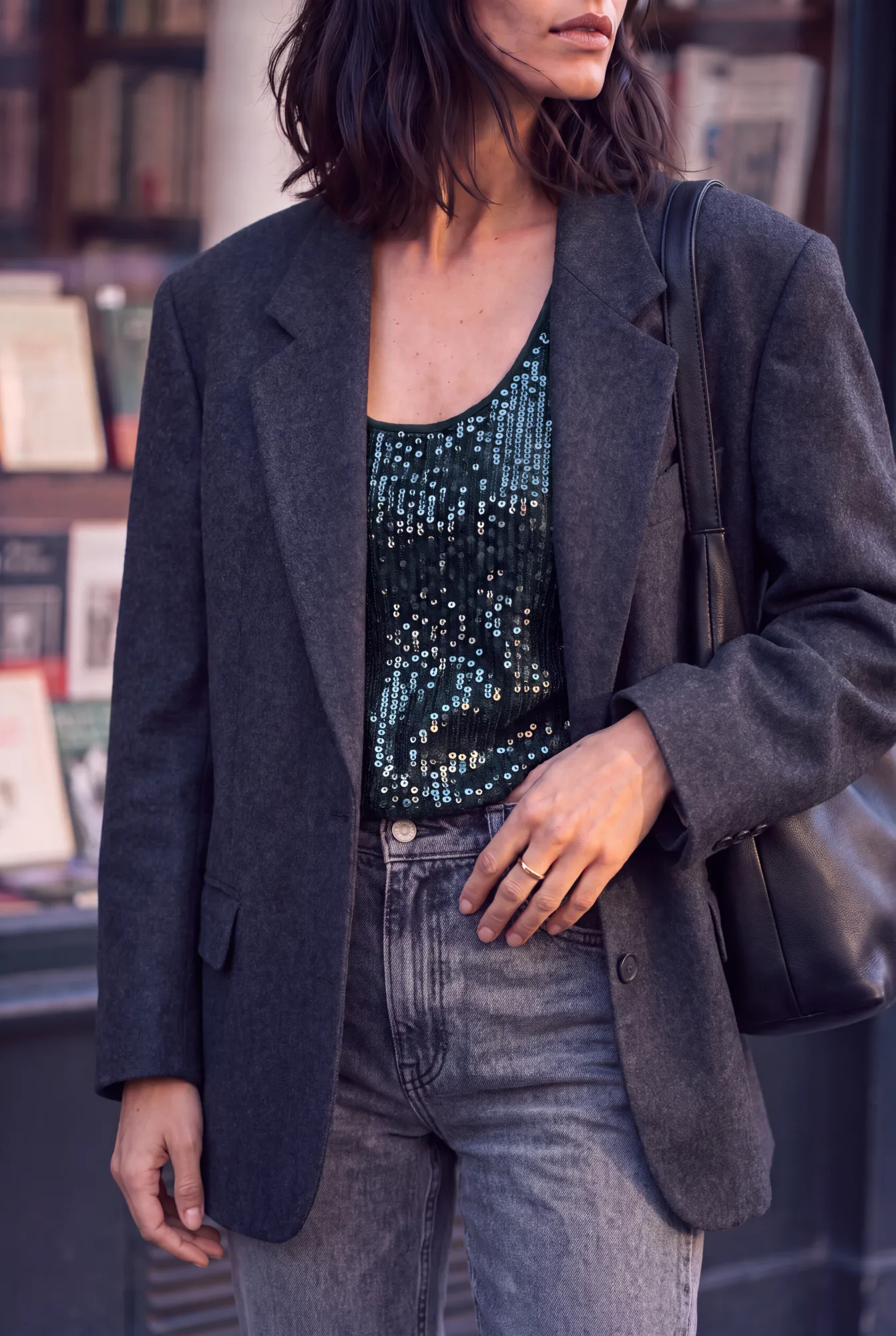 A woman in an oversized charcoal grey wool blazer over a dark sequin top and washed grey jeans, carrying a black bag | After the Toast, Relover