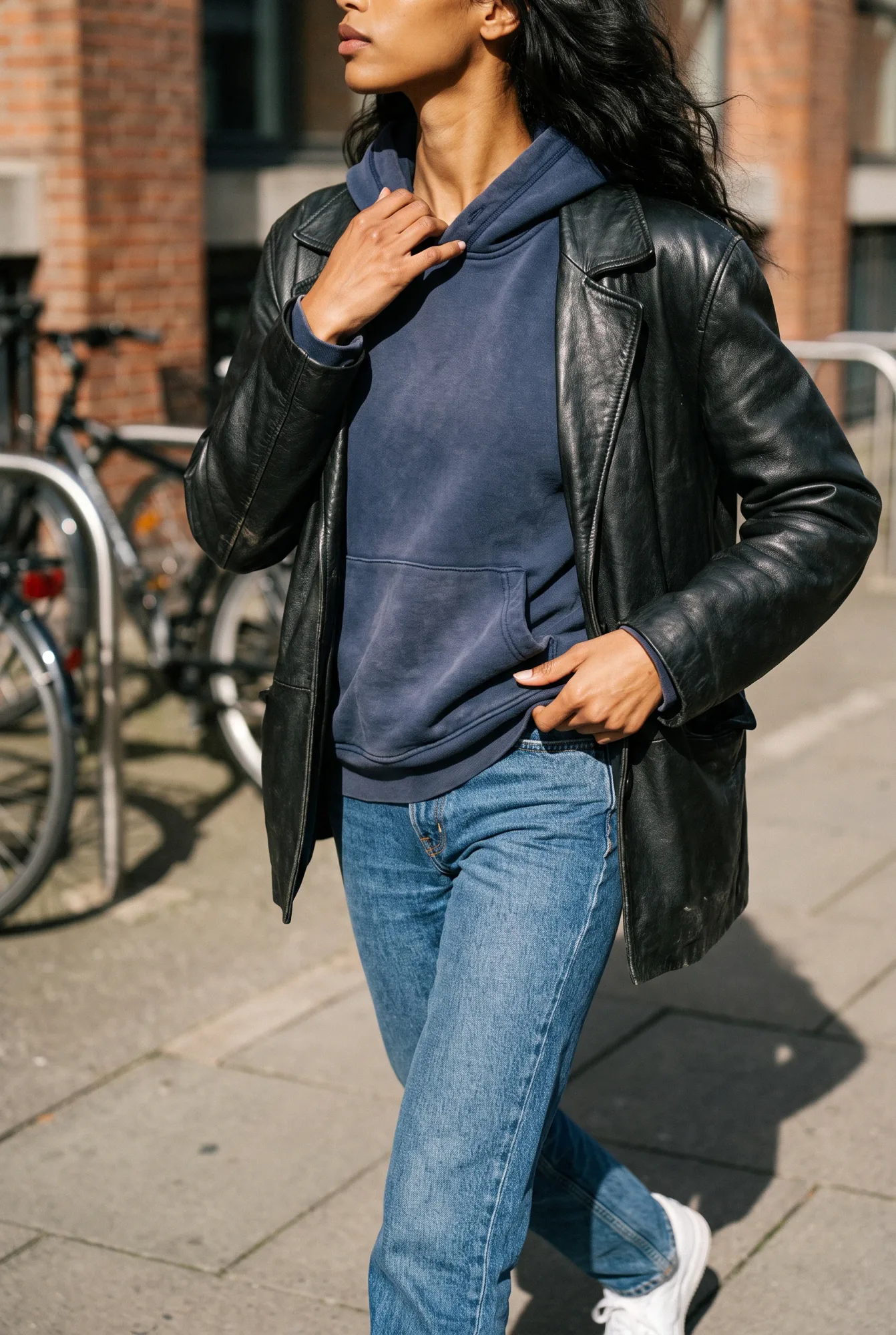 A woman with dark wavy hair walks on a street wearing an ink navy pullover hoodie layered under an open black leather | The Borrowed Hood, Relover