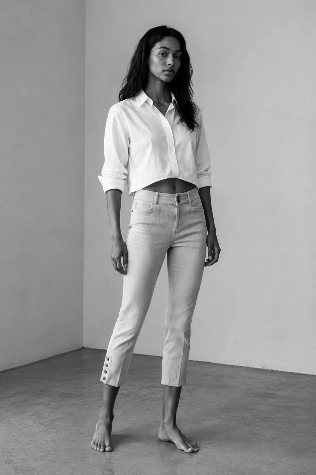 Black-and-white studio portrait of a woman wearing a white cropped shirt and light capri trousers.