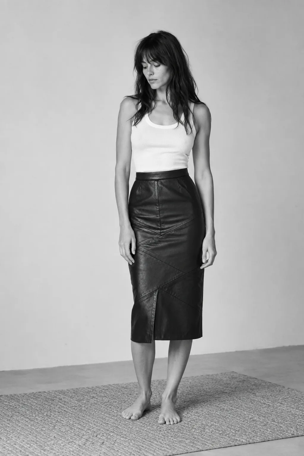 Black-and-white studio portrait of a woman wearing a white tank top and black leather pencil skirt.