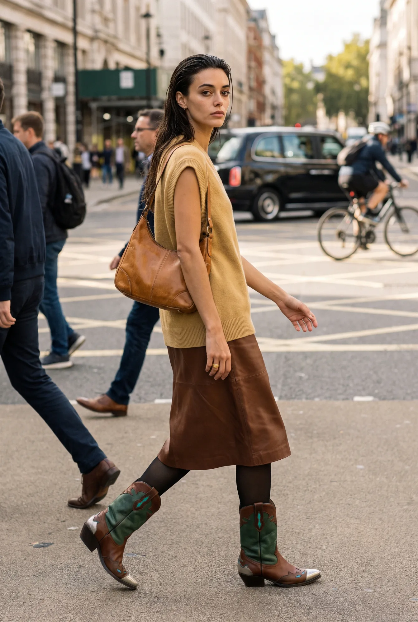 A woman in a mustard sweater vest and brown leather skirt crosses a London street wearing brown-and-green two-tone Western boots | The Long Way West, Relover