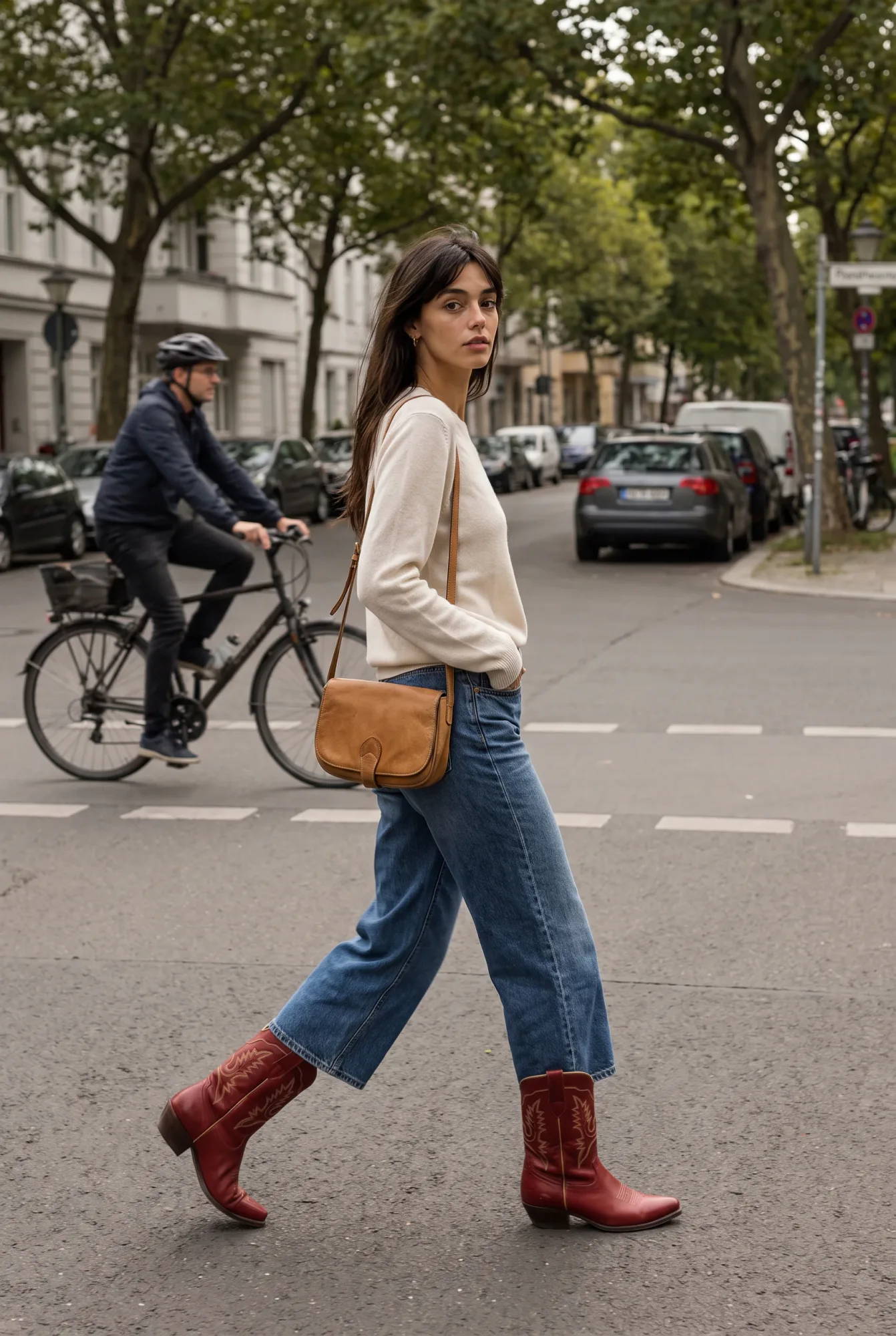 A woman in a cream sweater and wide-leg jeans with a crossbody bag walks across a city street past a cyclist, wearing Western boots | The Long Way West, Relover