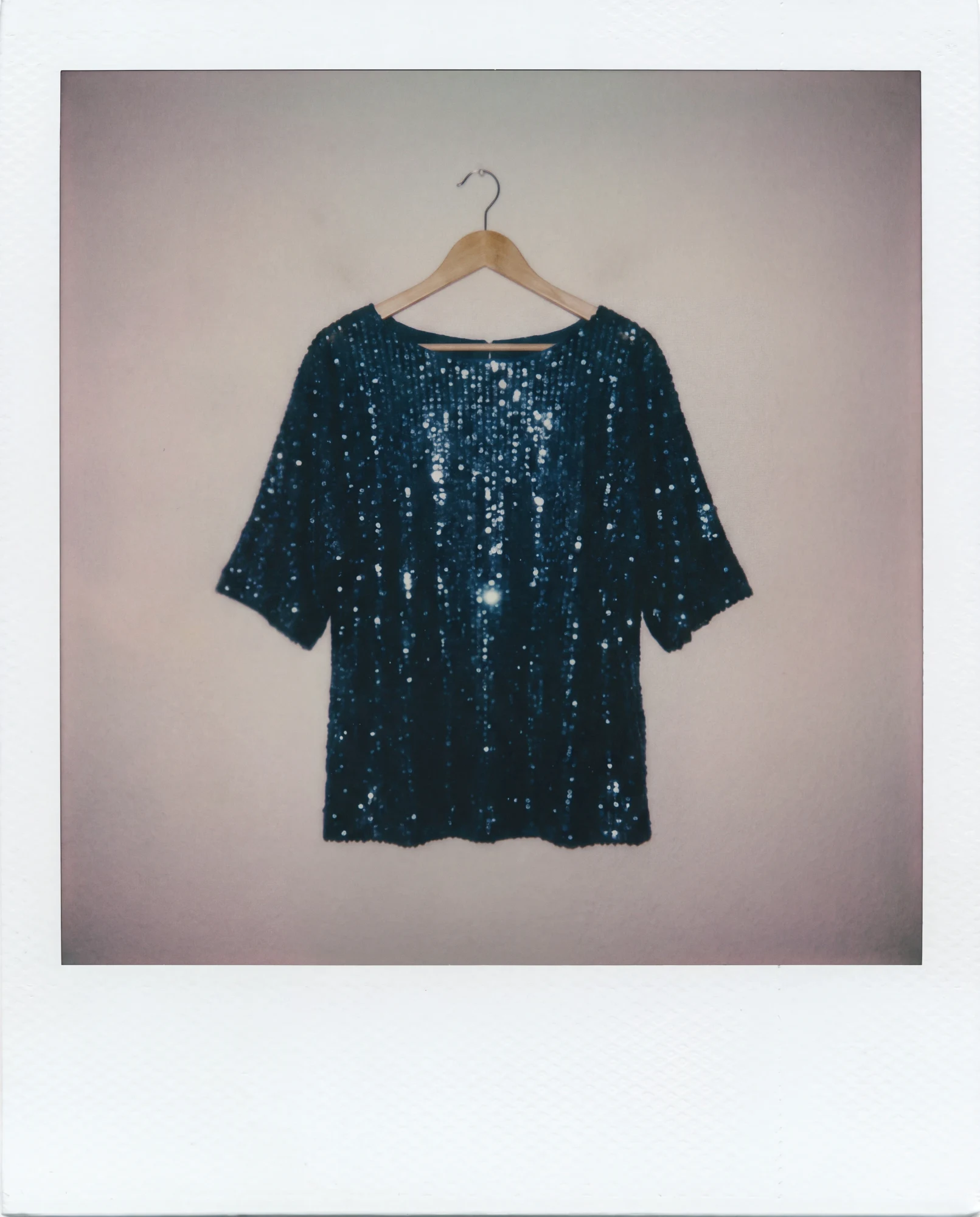Petrol-blue sequin top with a boat neckline and short, wide sleeves on a wooden hanger.