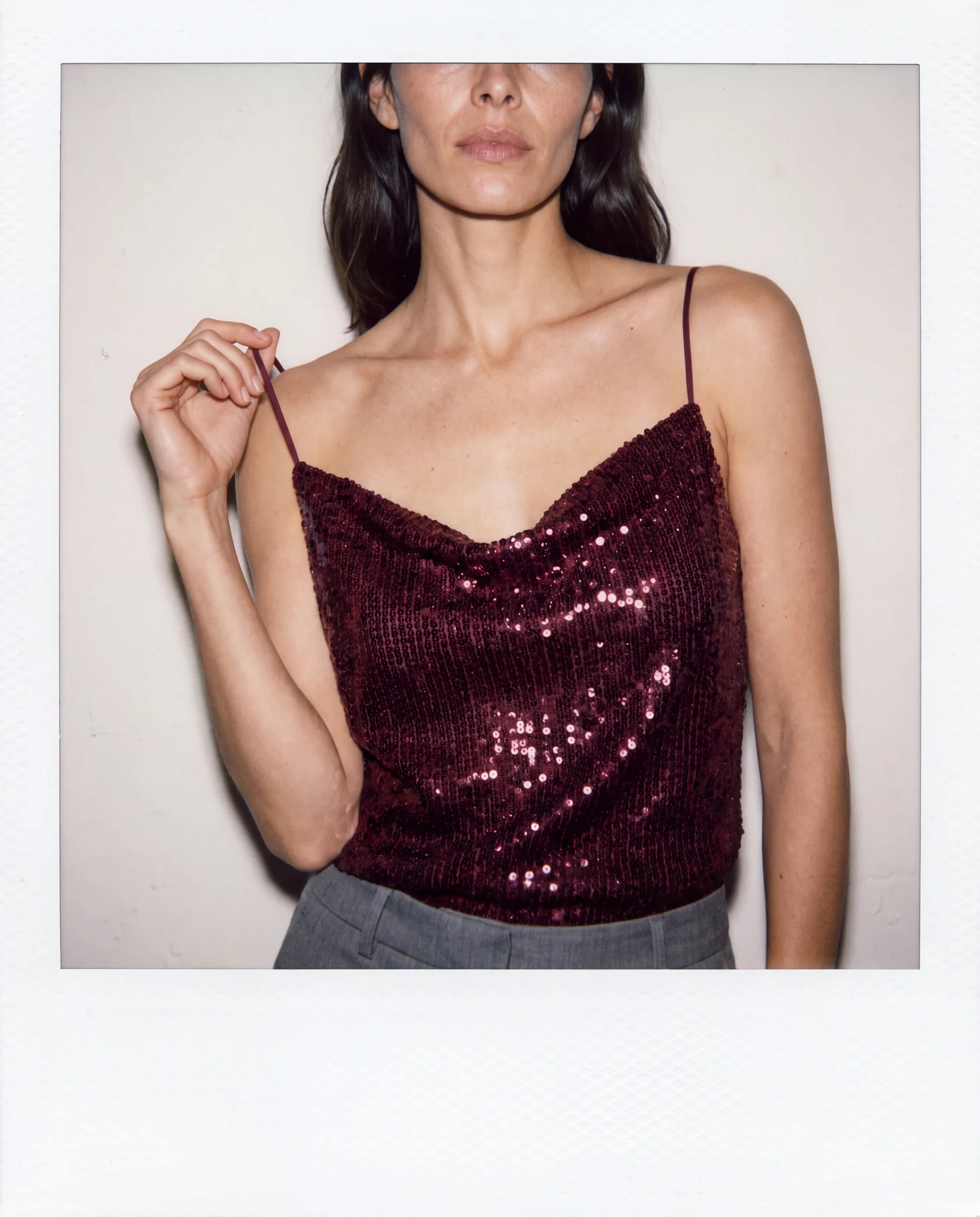 Close-up of a burgundy sequin camisole, with a hand gently holding one strap.